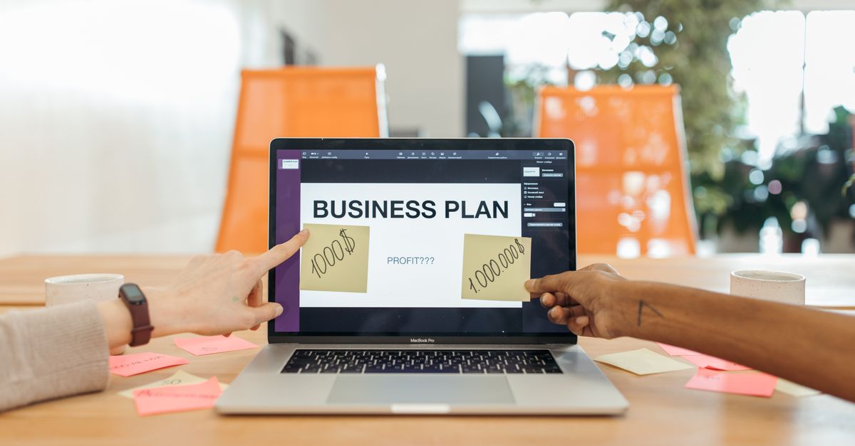 Two professionals strategizing a business plan on a laptop with sticky notes and profit goals.
